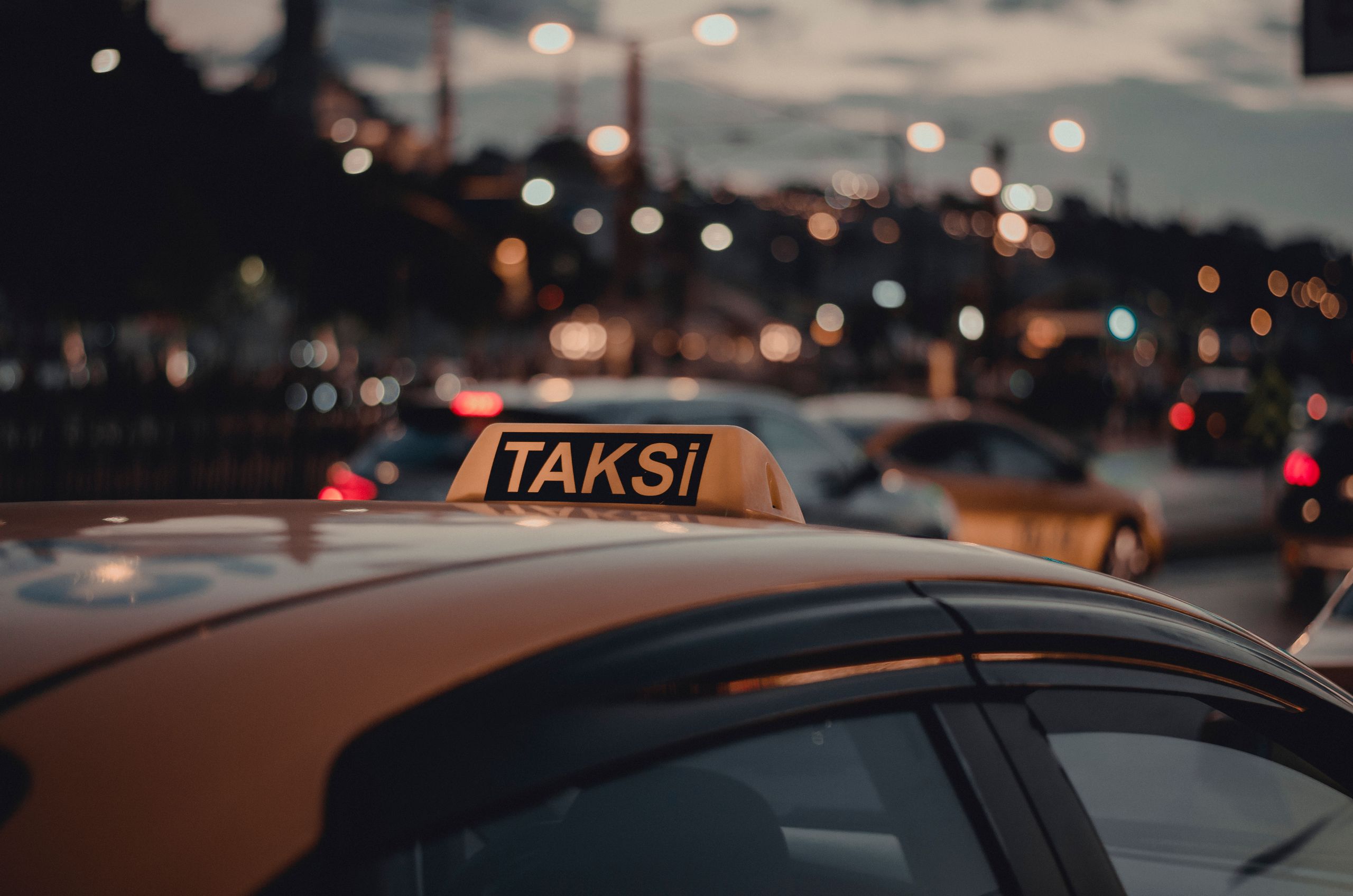 Close-up of a taxi with a 'Taksi' sign on a busy Istanbul street at night with bokeh lights.